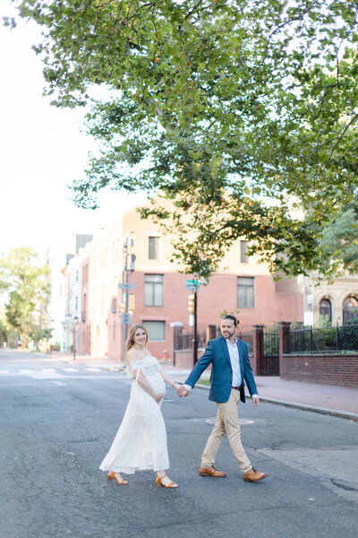 Couple walk across a Philadelphia street during maternity portrait session