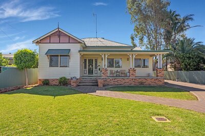 Cottage-style family home exterior featuring a wraparound front verandah, brick steps, and manicured lawn under clear daylight.