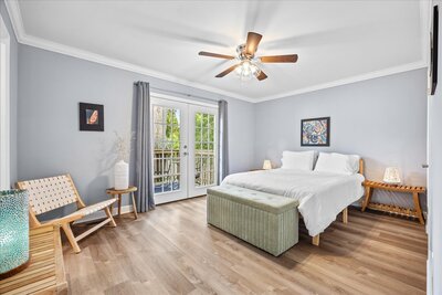 Stylish bedroom with wood flooring, ceiling fan, French doors leading to a deck, and a cozy seating bench at the foot of the bed.