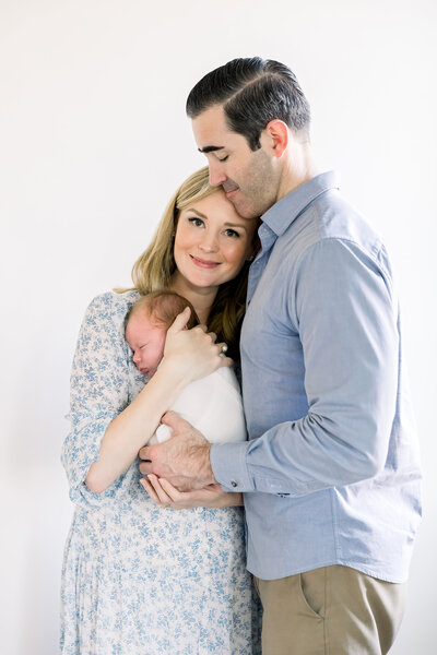 Image of new parents and newborn baby, mother holding her baby and cuddling with father, smiling at camera taken by Sacramento Newborn Photographer Kelsey Krall Photography