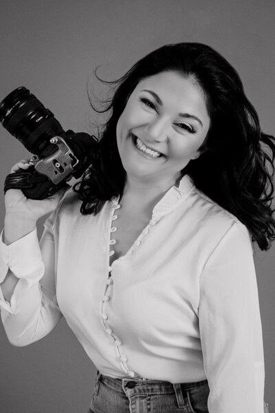 Black and white business headshot of Dana holding a camera