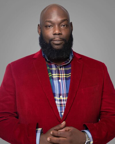 Business headshot of Red wearing a suit, photographed against a smooth gray background with soft directional lighting by Liza Hondros Photography.