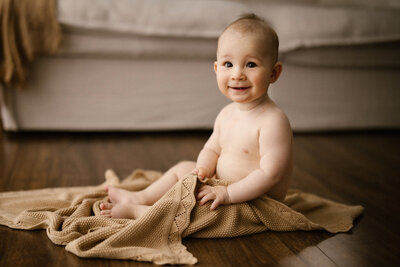 baby kit holding a blanket sitting on the floor during his baby photoshoot with aimee kelly photography in new plymouth