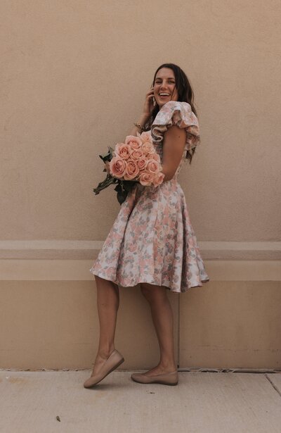 Claire in a pink floral dress holding a pink rose bouquet