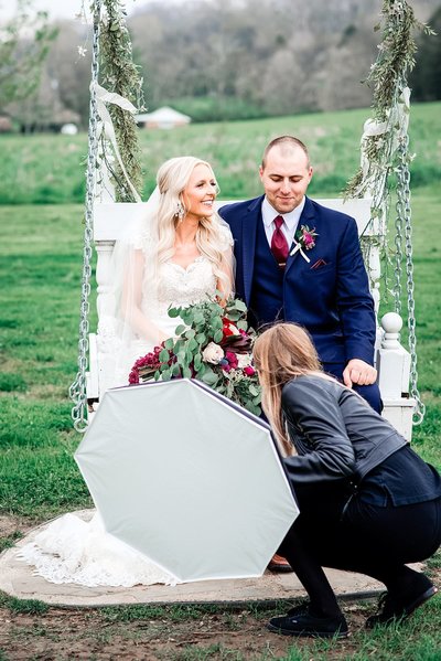 Photography Assistant adjusting brides dress on the swing at Drakewood Farms while holding a lighting box
