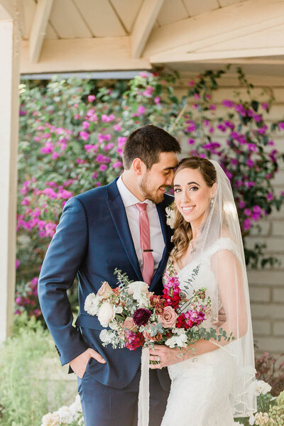 bride looking at camera while groom nuzzles into her at their timeless southern california wedding