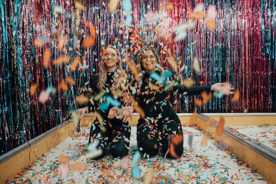 Two women surrounded by confetti and streamers. Showing the positive experience that graduating can be with the help of group therapy for college students in Manhattan. With guidance from a therapist and peer support your senior year could be the best year yet.