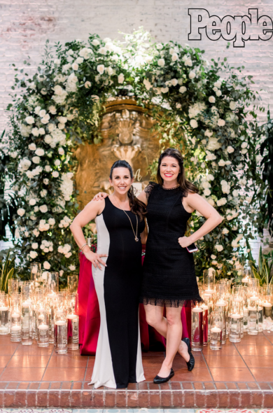 Event planners stand in front of floor candles and large floral archway at a wedding