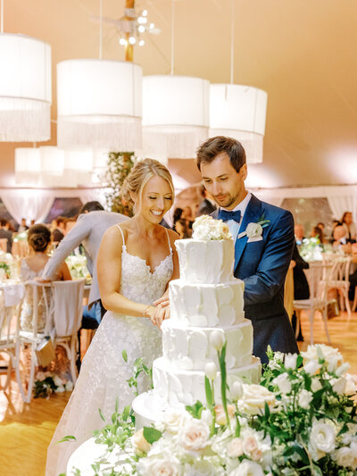 Bride and groom smiling and cutting their white tiered wedding cake
