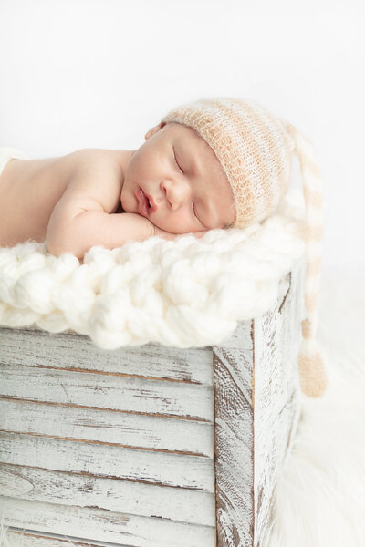 newborn baby boy with stripe floppy cap sleeping on his belly on cream knitted fabric for studio posed newborn portrait