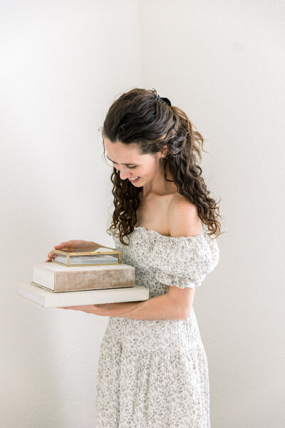 Photo of Sacramento Family Photographers Kelsey Krall holding two heirloom albums and a glass print box and smiling down