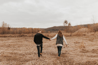 Couple holding hands walking through a field during their midwest engagement session