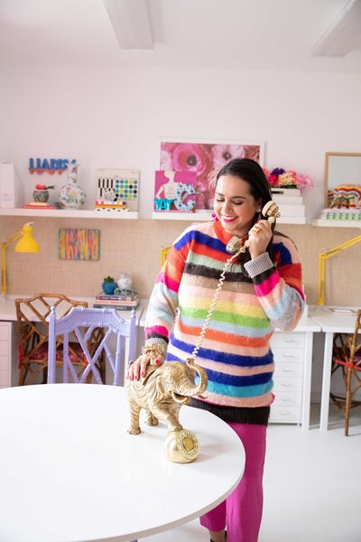 A woman in a rainbow sweater talking on a gold elephant telephone.