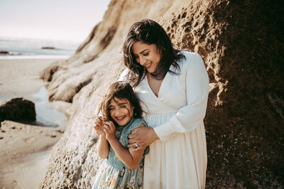 Norma and her daughter embrace each other while leaning on a rock at Hug Point, OR.