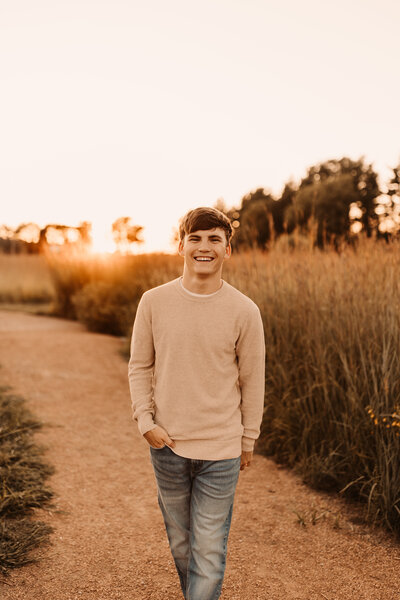 male senior in a prairie at sunset wearing a tan sweater