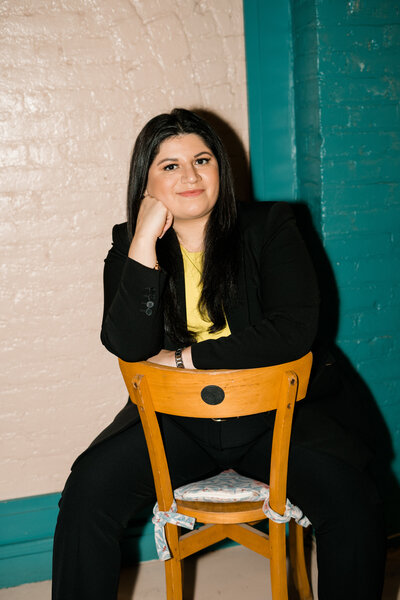 woman straddling wooden chair with hand resting under chin and smiling