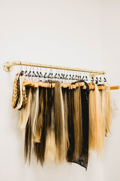 hair extensions hanging from a gold rack on a wall