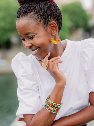 a black woman looking down and smiling with afraican jewelry and a white top