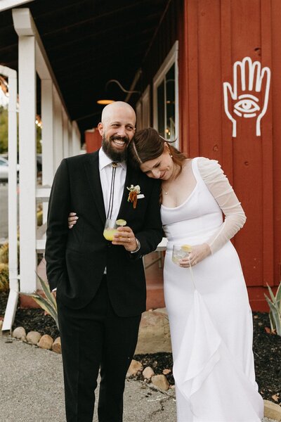 bride leans on grooms shoulder with drink in hand