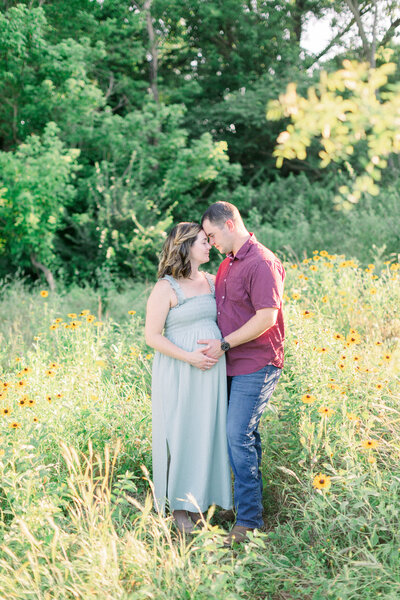 A mom and dad to be pose in a sunny field