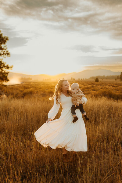 Mom holding her baby boy while dancing in her white flowy dress during sunset in the Truckee mountains