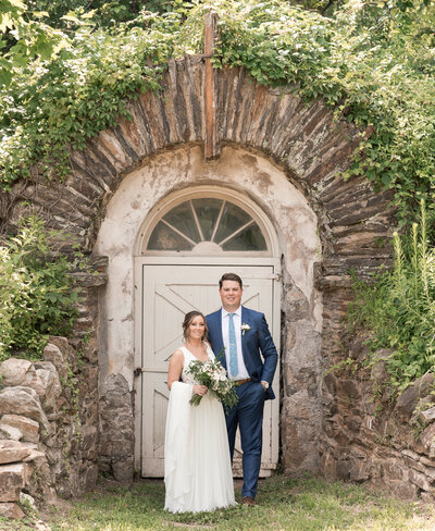 Bride and Groom standing in front of a  door surrounded by stone