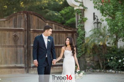 Bride and Groom walk hand in hand while looking at each other at the Rancho Las Lomas wedding venue in Silverado, CA