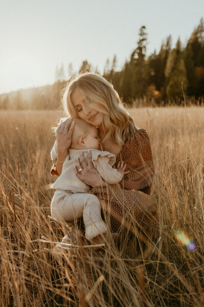 A woman holding a baby in a field at sunset.