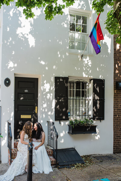 Two brides in white wedding gowns staring into each other’s eyes in front of a stoop in philadelphia.