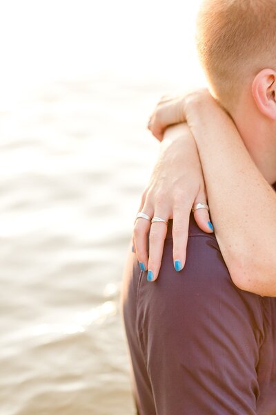 Woman's hand rests on fiancee's shoulder as they stand in Lake Minnetonka.