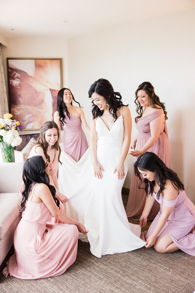 A bride and her bridesmaids helping each other with their dresses.