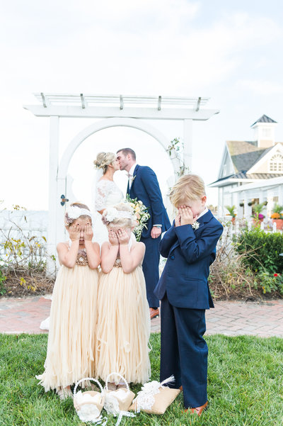 Flower girls and ring bearer cover eyes while bride and groom kiss
