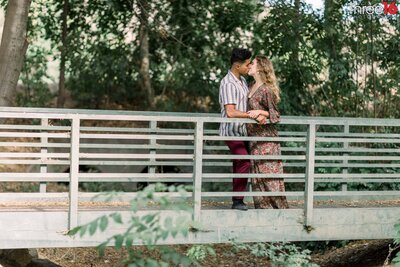 Engaged couple share a kiss while standing on a bridge at the Frank G. Bonelli Regional Park engagement session