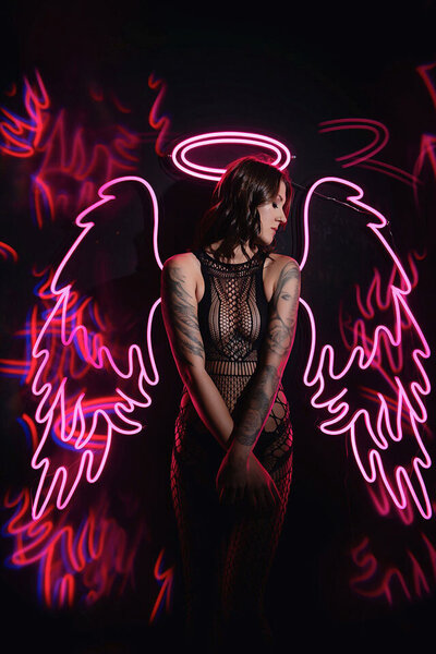 Tattoeed woman posing with neon wings and halo