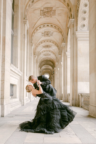 a bride in a black dress being dipped in the halls of the louvre in paris