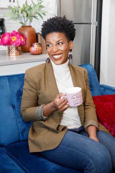 Woman sitting on a blue couch holding a pink mug, wearing a blazer