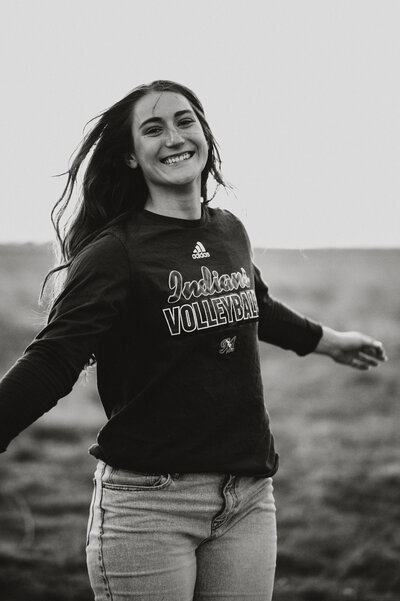 Senior girl spins in a tee of the college she will be attending in black and white photo
