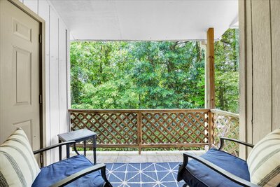 Peaceful balcony with wooden lattice railing, outdoor seating, and lush green forest views.