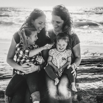 Bay Area LGBTQIA family portrait of Lesbian moms and two daughters laughing together on California beach.