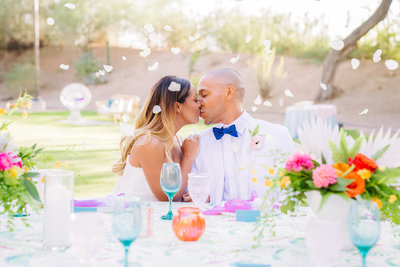 bride and groom wearing white kissing at head table