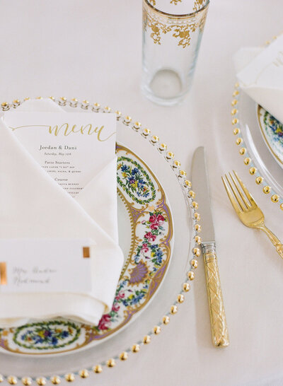 close up of gold-trimmed table setting and wedding invitation