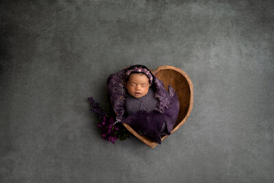 Newborn baby wrapped in purple in a heart bowl