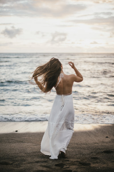 Woman wearing white dress walking on beach toward ocean