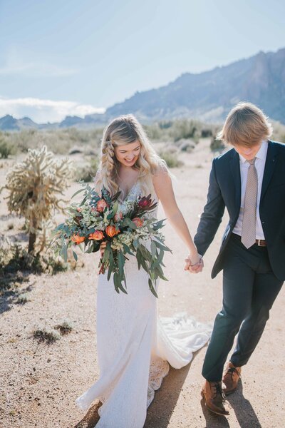 Lake Tahoe Photographer Bride and groom hold hands as she holds bouquet in desert