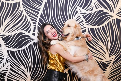 girl holding a golden retriever in front of a black and gold damask backdrop posing for a photo booth photo