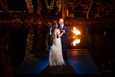 Bride and groom dancing on the dock of the lake at night with twinkle lights and trees at Lake Oak Meadows wedding venue in Temecula.