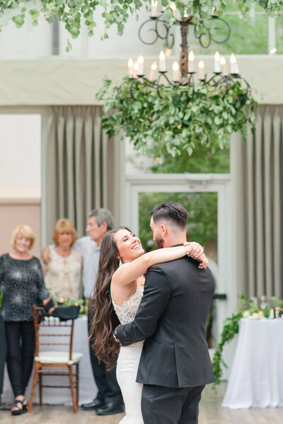 Bride and groom dance under a chandelier covered in greenery during their Vail wedding reception.