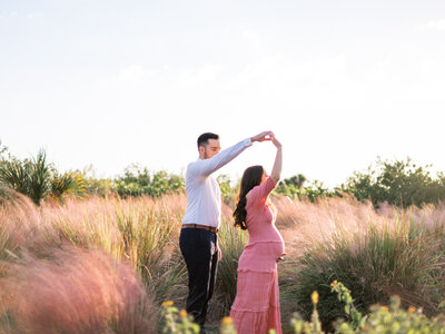 husband twirling pregnant wife in a field