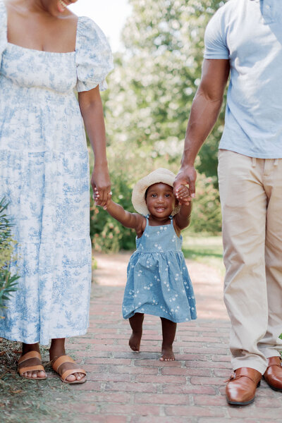 Outdoor family portrait session of parents holding little girl's hands while walking