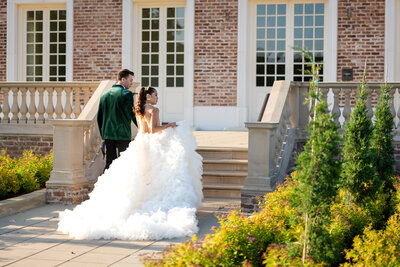 Bride and Groom on a Country Club Golf Course in Virginia. Embracing and naturally posing while looking  in the direction of the camera.  Bride in white with a long veil.  Groom in Black pants, white jacket and forest green vest.  Epic clouds during sunset in the background.